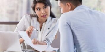 A man and a woman sit at a table with a laptop and review a document