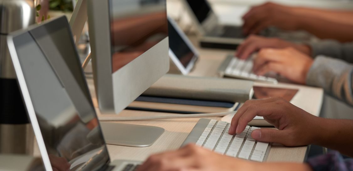 Hands using a keyboard on a desktop computer and a laptop