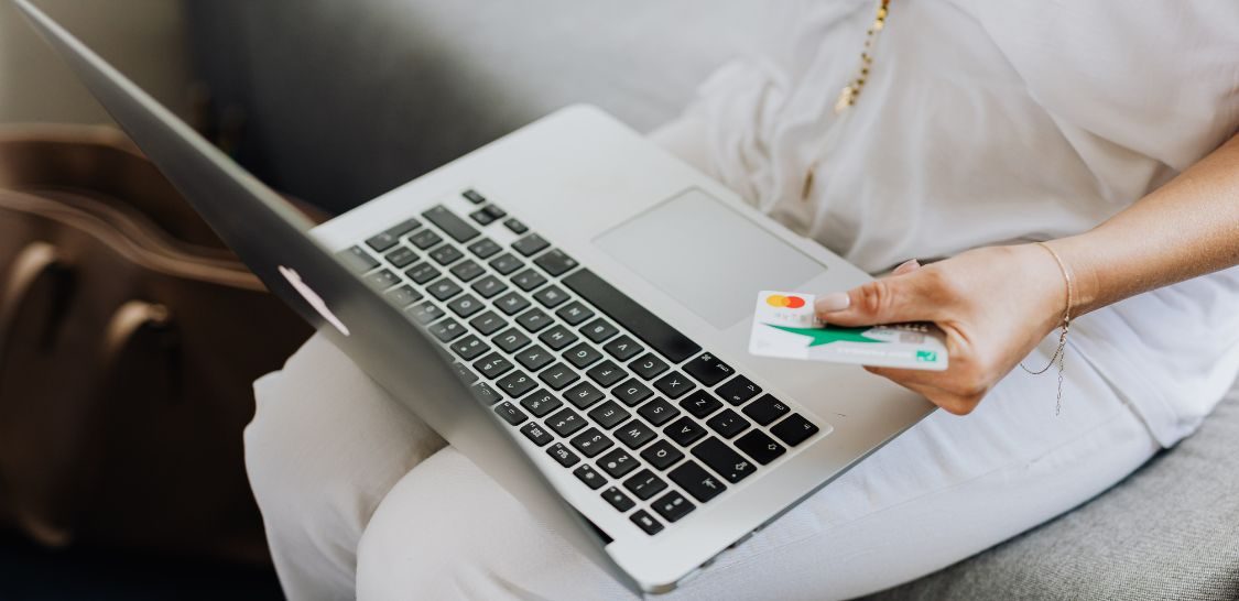 a person wearing white with a laptop on their lap holding a credit card as if they are paying for something online