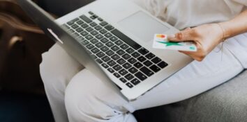 a person wearing white with a laptop on their lap holding a credit card as if they are paying for something online