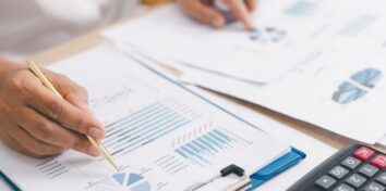 A person works on financial documents at a desk with a calculator