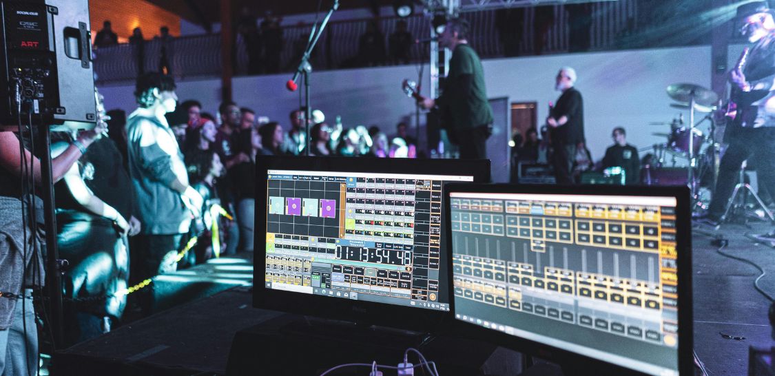 Musicians playing for a crowd and sound equipment displaying stats on screens.