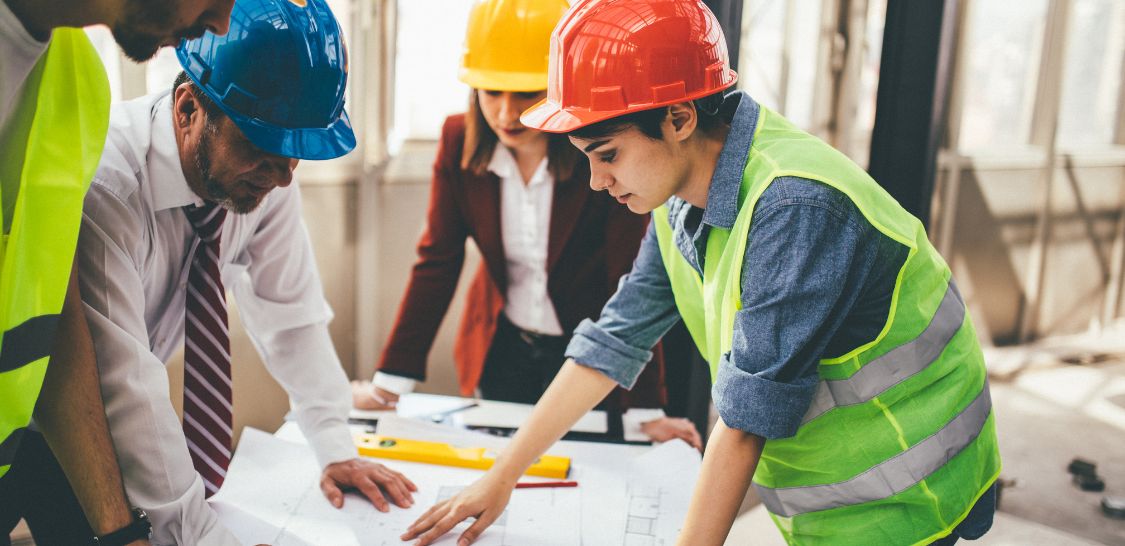 A group of people wearing hard hats stand around a table looking at construction plans
