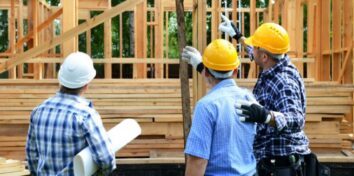 three men in hard hats stand in front of a home being built.