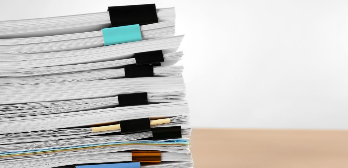 A pile of documents, multiple different sections bound together by clips, sit on a table