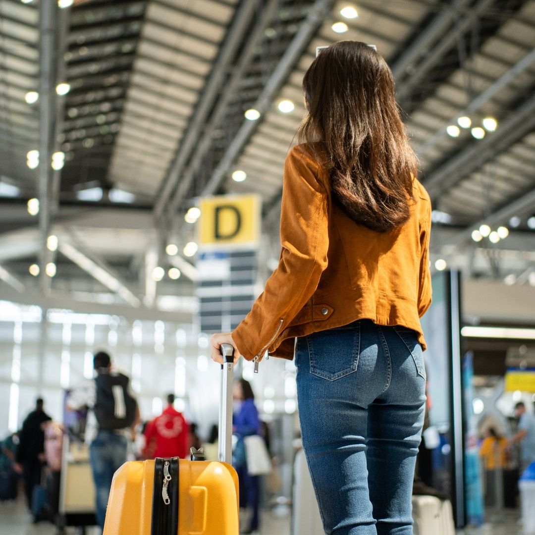 Person walking through an airport with a rolling suitcase.