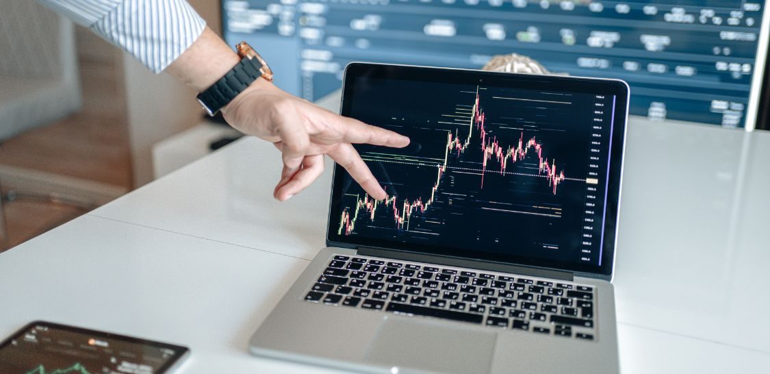 A hand points at a computer screen that shows a stock market graph