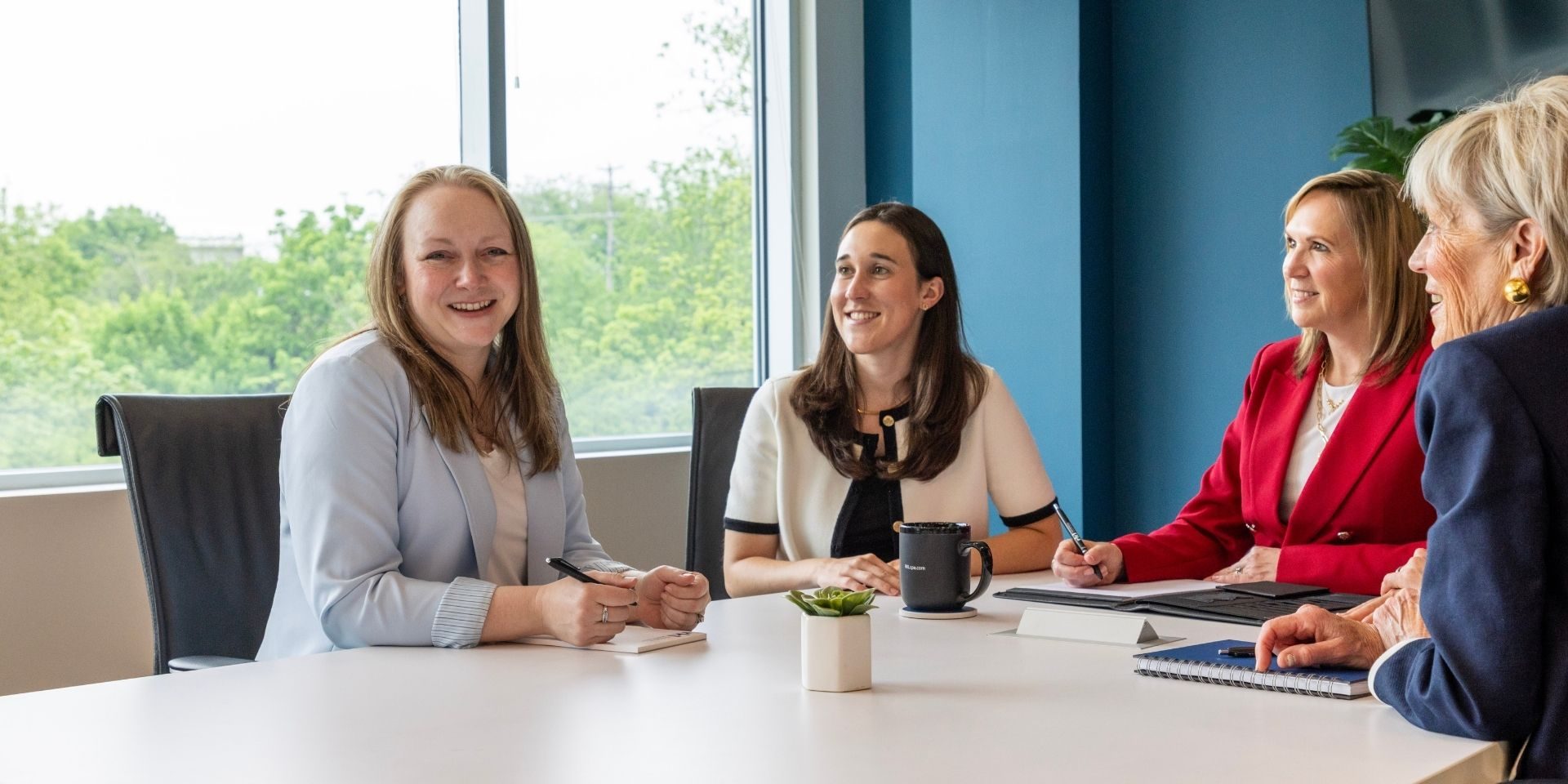 Four professionals meeting around a conference table in a modern office, reviewing notes and discussing business services.