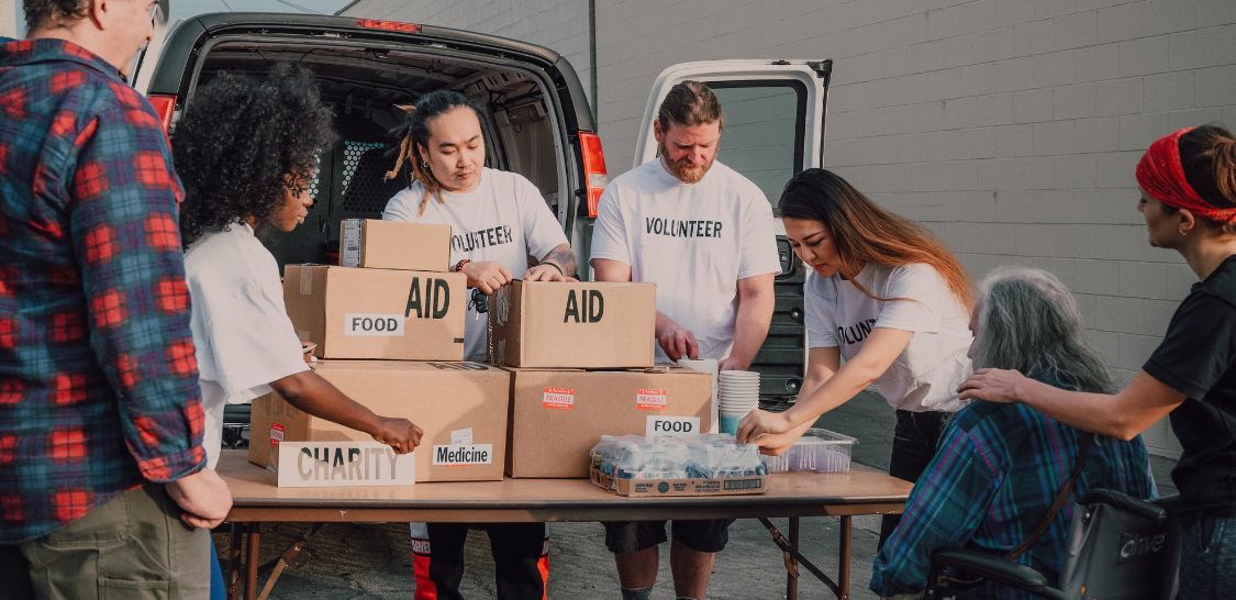 A group of volunteers hand out boxes that are labeled as food and aid to people on the street