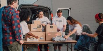 A group of volunteers hand out boxes that are labeled as food and aid to people on the street