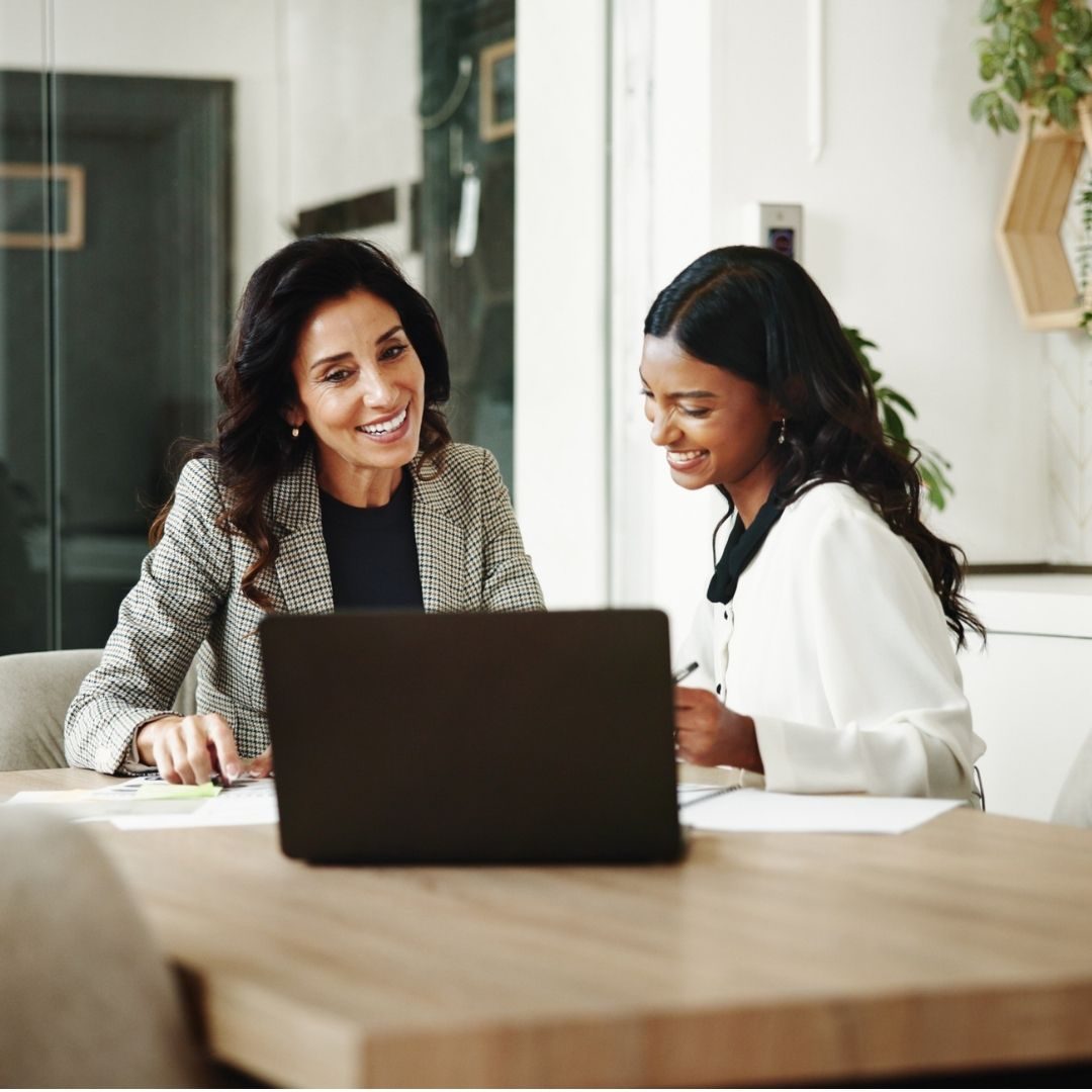 Two tax professionals reviewing documents together on a laptop in a bright office