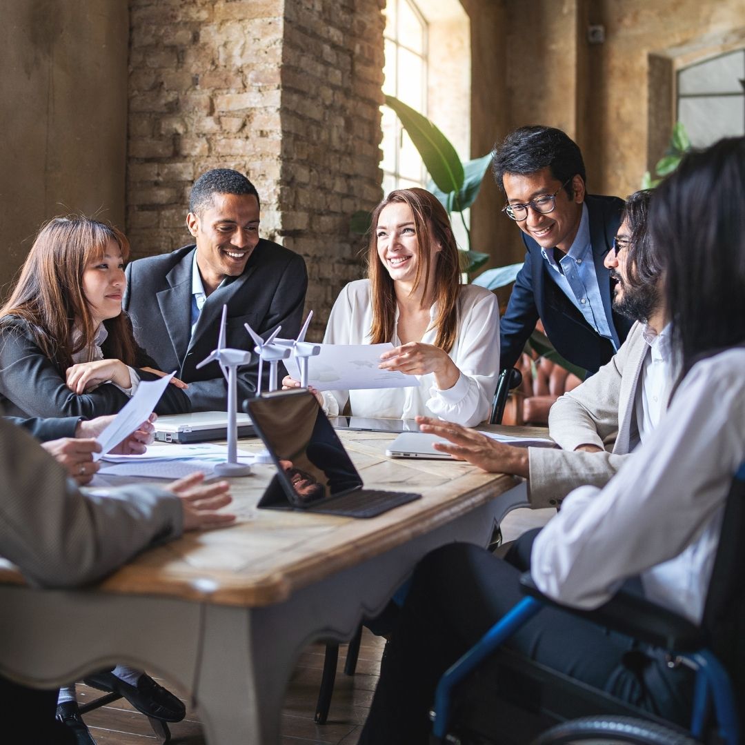 A diverse team reviews documents and collaborates around a conference table with wind turbine models.