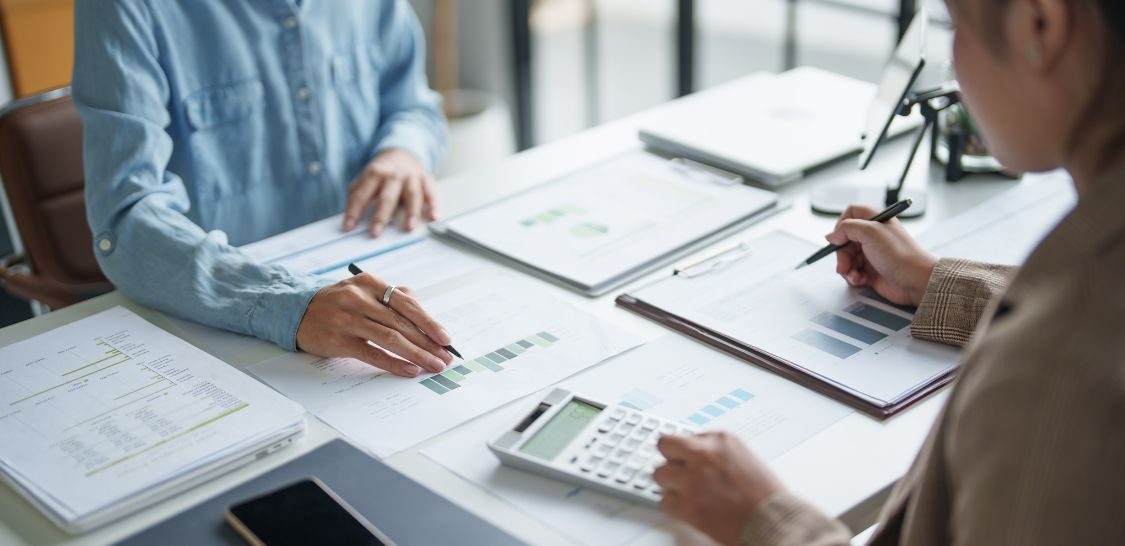 Three professionals review financial reports and calculations at a desk.