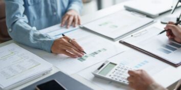Three professionals review financial reports and calculations at a desk.