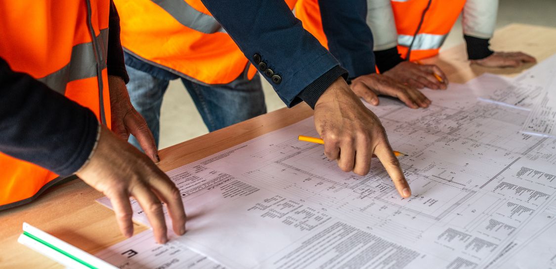 Construction professionals in safety vests review building plans at a worktable.