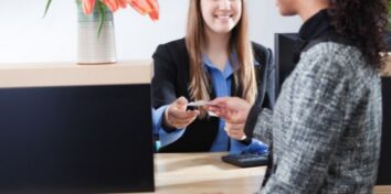 A credit union representative hands a card or document to a member across a service desk.