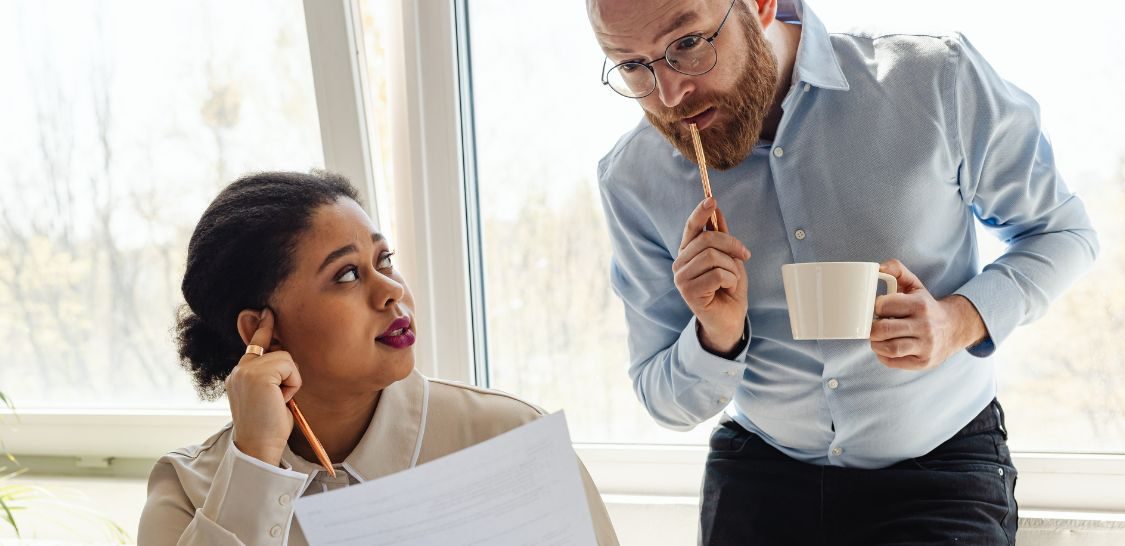 Two professionals discuss a document while reviewing workplace information in an office.