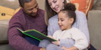 Parents and young child read a book together at home.