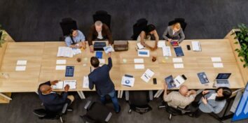 Overhead view of a diverse team meeting around a conference table, reviewing financial documents, charts, and laptops.