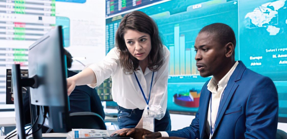 Two financial professionals review market data on computer screens in a trading office.