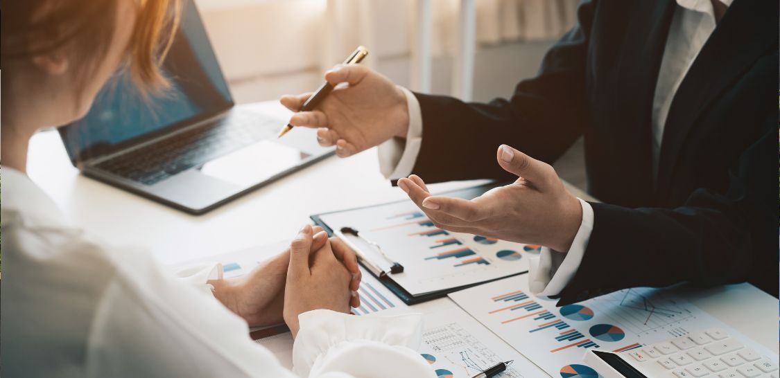 Business professionals review financial charts and documents during an acquisition diligence meeting.