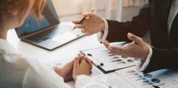 Business professionals review financial charts and documents during an acquisition diligence meeting.
